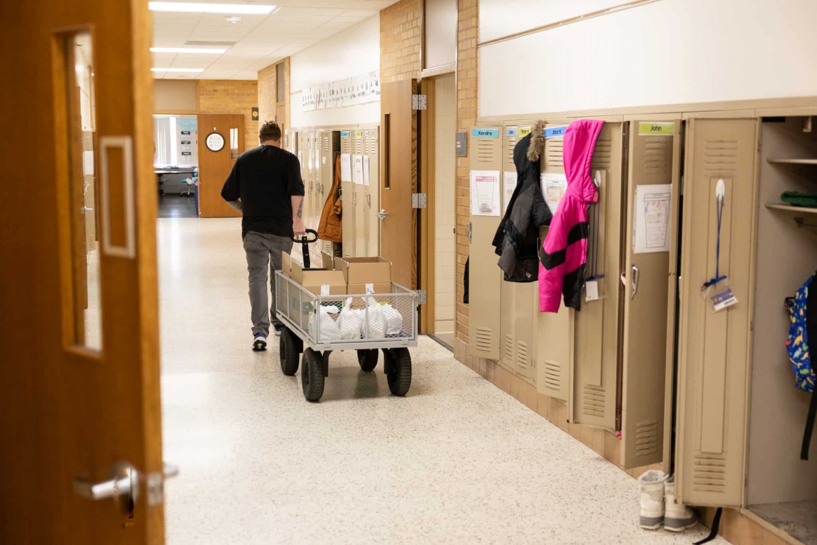 Distribution volunteer walking down hallway with food boxes during food bag distribution at Monroe in April 2023