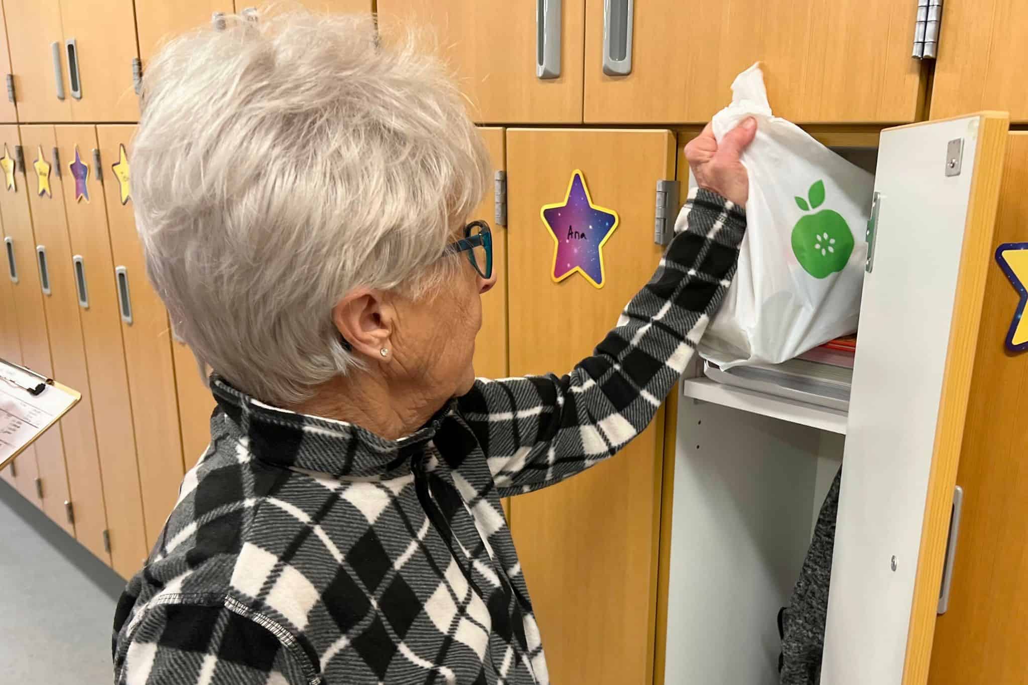 Food Distribution volunteer placing green food bag in child's backpack in Worthington, MN