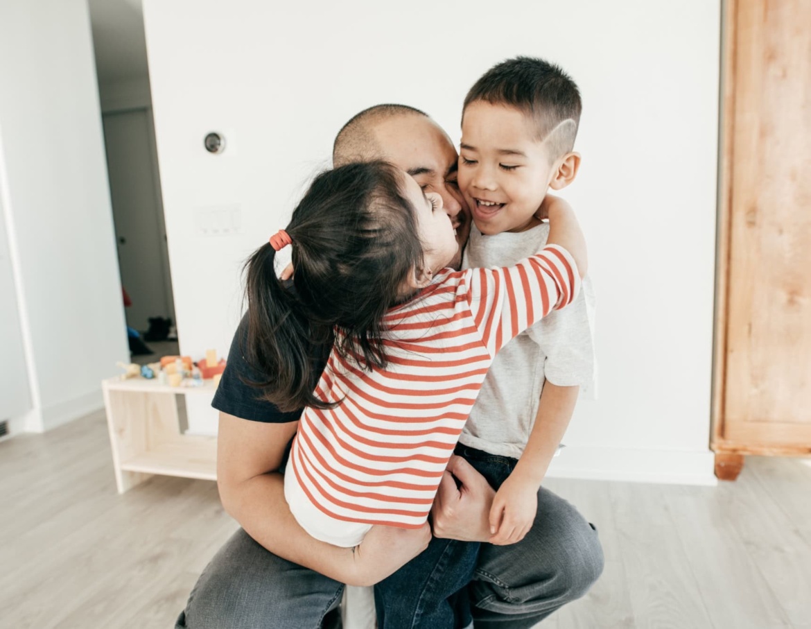 Two young children hugging their dad in their home